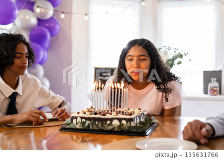 Teen girl blowing out candles on birthday cake at family celebration 135631766