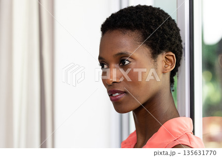 Confident woman in coral blouse looking thoughtfully out window at home Confident woman in coral blouse looking thoughtfully out window at home 135631770