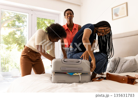 Packing suitcase on bed, African American women preparing for travel adventure together 135631783