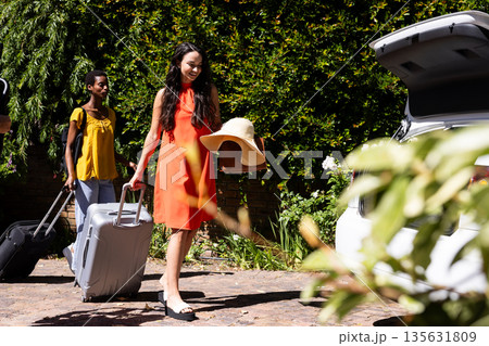 Friends packing car with luggage for road trip, smiling and enjoying sunny day Friends packing car with luggage for road trip, smiling and enjoying sunny day 135631809
