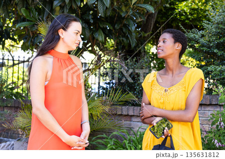 Two female friends talking outdoors, enjoying conversation in sunny garden 135631812