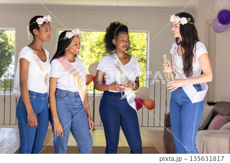 Celebrating bachelorette party, diverse female friends wearing sashes and floral crowns Celebrating bachelorette party, diverse female friends wearing sashes and floral crowns 135631817