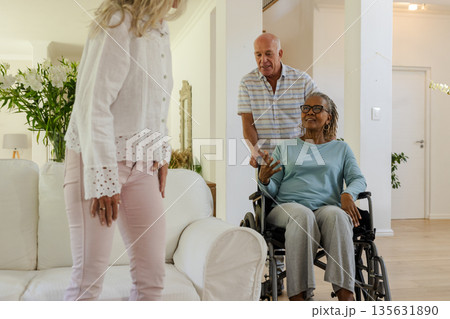 Senior friends enjoying conversation at home, one woman in wheelchair smiling warmly Senior friends enjoying conversation at home, one woman in wheelchair smiling warmly 135631890