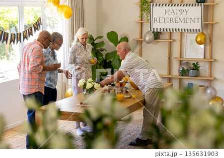 Senior friends celebrating retirement with drinks and snacks at home gathering Senior friends celebrating retirement with drinks and snacks at home gathering 135631903