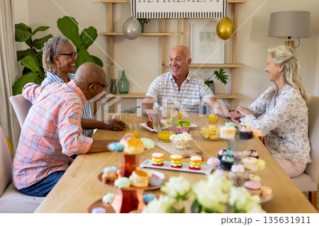 Senior friends enjoying retirement party with laughter and colorful cupcakes at home 135631911