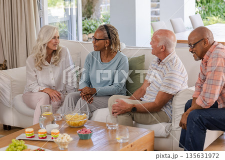 Senior friends enjoying conversation and snacks together in cozy living room 135631972