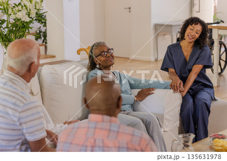 In living room, caregiver engaging with senior friends, sharing joyful conversation In living room, caregiver engaging with senior friends, sharing joyful conversation 135631978