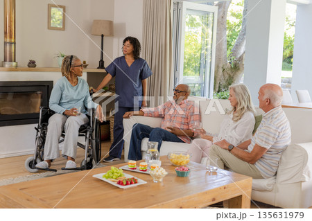 Senior friends enjoying conversation with caregiver in cozy living room setting 135631979