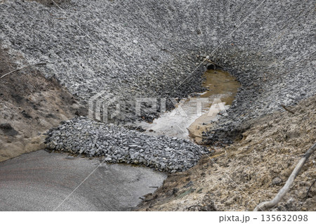 Water trickles through a dry river bed surrounded by rocky terrain and dirt, with evidence of erosion visible on the banks during the day 135632098