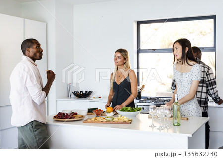 In kitchen, friends preparing food and chatting while gathering around counter In kitchen, friends preparing food and chatting while gathering around counter 135632230
