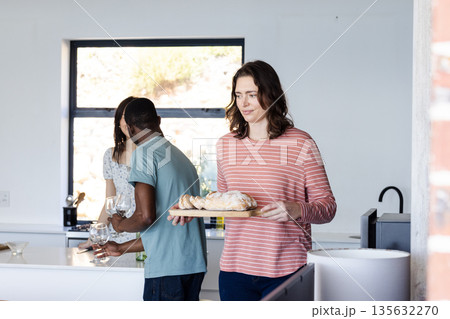 Friends preparing meal together in kitchen, carrying bread and setting table 135632270