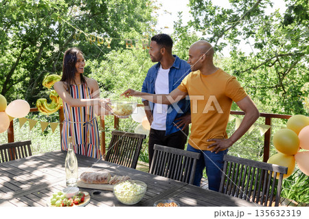 Friends enjoying outdoor party, sharing snacks and smiling in sunny garden 135632319