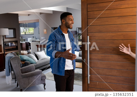 African American man welcoming guest at home, smiling and opening door warmly 135632351