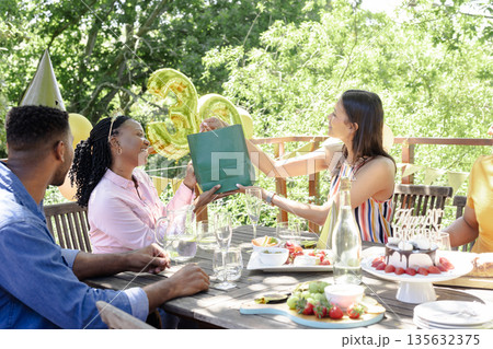 Celebrating outdoors, friends exchanging gifts at birthday party with joyful smiles Celebrating outdoors, friends exchanging gifts at birthday party with joyful smiles 135632375