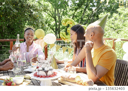 Celebrating birthday outdoors, friends enjoying cake and drinks on sunny day 135632403