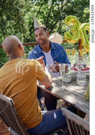 Celebrating birthday outdoors, friends wearing party hats and holding balloons, chatting 135632404