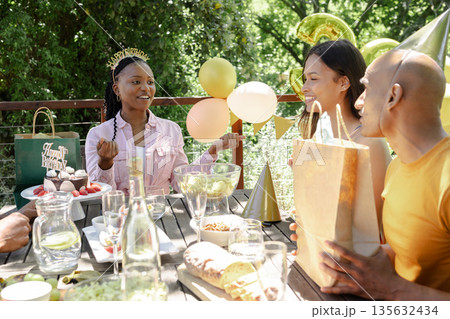 Celebrating birthday outdoors, friends with cake, balloons, and party hats together Celebrating birthday outdoors, friends with cake, balloons, and party hats together 135632434