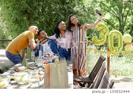 Friends celebrating 30th birthday outdoors, taking selfie with golden balloons Friends celebrating 30th birthday outdoors, taking selfie with golden balloons 135632444