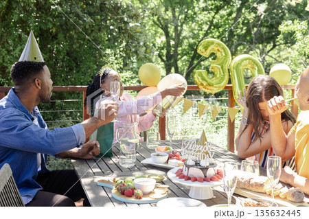 Celebrating birthday outdoors, friends sharing champagne and cake in festive atmosphere 135632445
