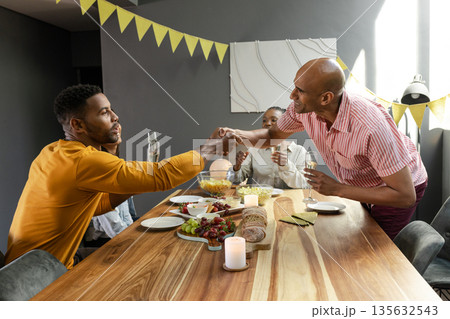 Friends celebrating at home, shaking hands over dinner table with candles and food Friends celebrating at home, shaking hands over dinner table with candles and food 135632543