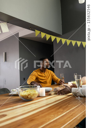 Man in yellow shirt enjoying dinner with friends, holding champagne glass 135632546