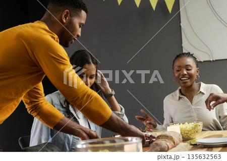 Friends enjoying dinner party, sharing food and laughter around festive table 135632563