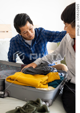 Father and son packing suitcase on bed, preparing for family trip together Father and son packing suitcase on bed, preparing for family trip together 135632605