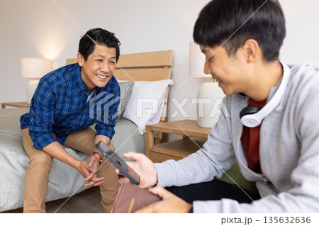 Father and son bonding at home, smiling and sharing smartphone together 135632636