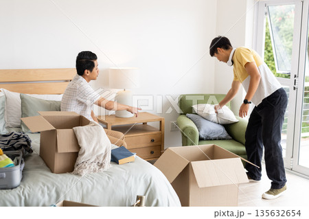 Friends unpacking boxes and organizing bedroom, creating cozy living space together Friends unpacking boxes and organizing bedroom, creating cozy living space together 135632654