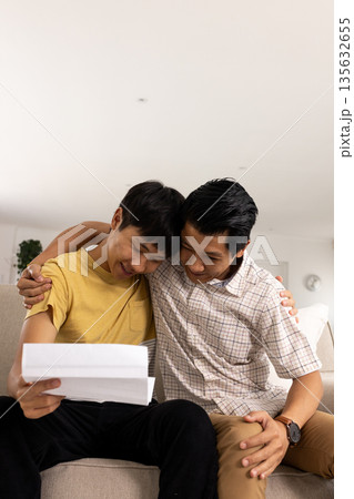 Father and son celebrating good news together while reading letter on couch Father and son celebrating good news together while reading letter on couch 135632655