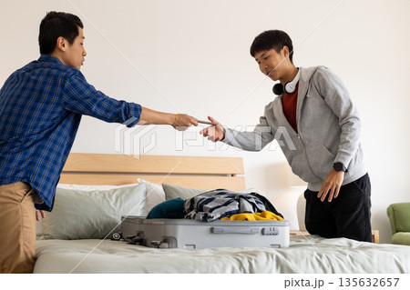 Friends packing suitcase together in bedroom, preparing for travel adventure 135632657