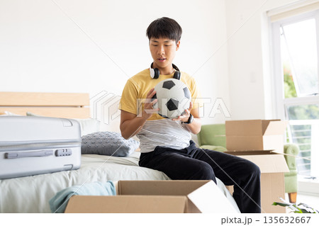 Unpacking boxes in bedroom, young man holding soccer ball with headphones 135632667