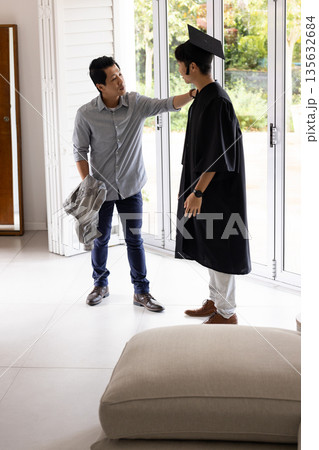 Father congratulating son in graduation gown at home, sharing proud moment together Father congratulating son in graduation gown at home, sharing proud moment together 135632684