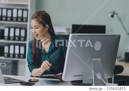 Determined asian businesswoman works late in a modern office, confidently analyzing data on her laptop, embodying success and professionalism with a smile Determined asian businesswoman works late in a modern office, confidently analyzing data on her laptop, embodying success and professionalism with a smile 135632855