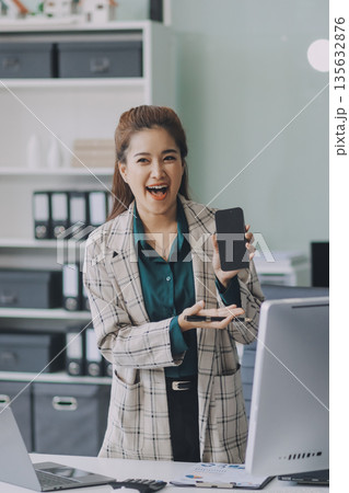 Determined asian businesswoman works late in a modern office, confidently analyzing data on her laptop, embodying success and professionalism with a smile 135632876