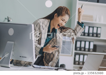 Determined asian businesswoman works late in a modern office, confidently analyzing data on her laptop, embodying success and professionalism with a smile Determined asian businesswoman works late in a modern office, confidently analyzing data on her laptop, embodying success and professionalism with a smile 135632880