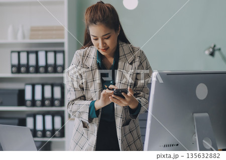 Determined asian businesswoman works late in a modern office, confidently analyzing data on her laptop, embodying success and professionalism with a smile Determined asian businesswoman works late in a modern office, confidently analyzing data on her laptop, embodying success and professionalism with a smile 135632882