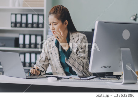 Pain, headache and stressed finance manager feeling sick, tired and worried about a financial problem at her startup company. Young and frustrated professional businesswoman working at an office 135632886