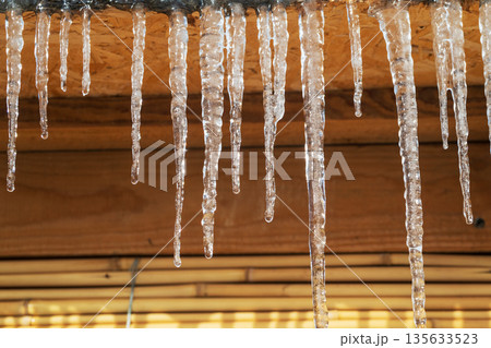Icicles hanging from a roof, they are clear and shiny 135633523
