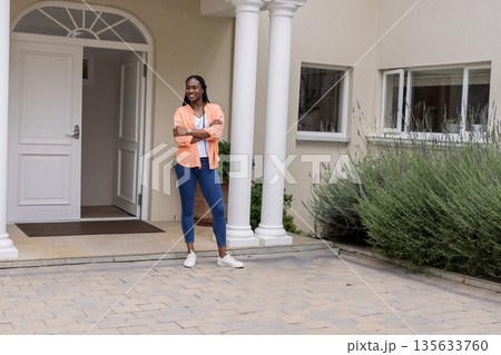 African American woman in 30s standing on stone pavers near potted plant, white door with columns 135633760