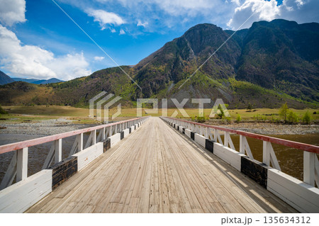 Wooden bridge over Chulyshman river in Altai Russia leading into scenic mountain valley Perspective view into remote wilderness Wooden bridge over Chulyshman river in Altai Russia leading into scenic mountain valley Perspective view into remote wilderness 135634312