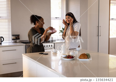 Friends exchanging gifts in modern kitchen, sharing joy and surprise together Friends exchanging gifts in modern kitchen, sharing joy and surprise together 135634421