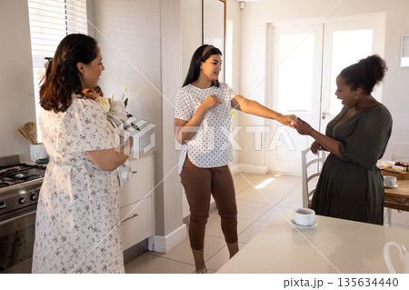 Friends in kitchen celebrating with laughter and conversation, holding baby 135634440