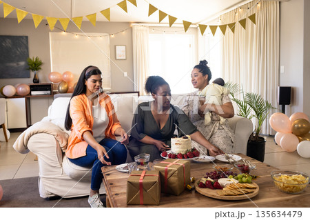 Women celebrating at home, enjoying cake and snacks with festive decorations Women celebrating at home, enjoying cake and snacks with festive decorations 135634479