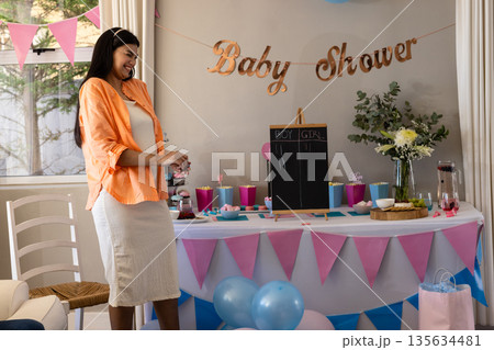 Expectant mother smiling at baby shower with gifts and decorations around Expectant mother smiling at baby shower with gifts and decorations around 135634481