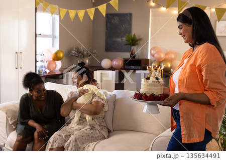 Celebrating at home, woman holding cake while friends enjoy joyful gathering Celebrating at home, woman holding cake while friends enjoy joyful gathering 135634491