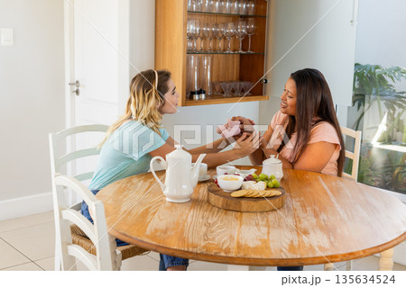 Two women enjoying tea and snacks at home, sharing joyful moment 135634524