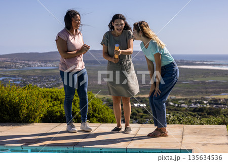 Friends celebrating by poolside with confetti popper, enjoying outdoor gathering 135634536
