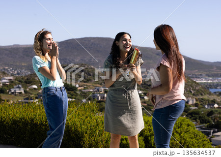 Women celebrating outdoors, laughing and holding gift with scenic mountain view 135634537
