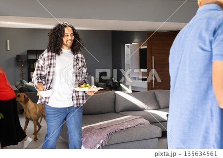 Man carrying plates with snacks at home during celebration, smiling happily Man carrying plates with snacks at home during celebration, smiling happily 135634561